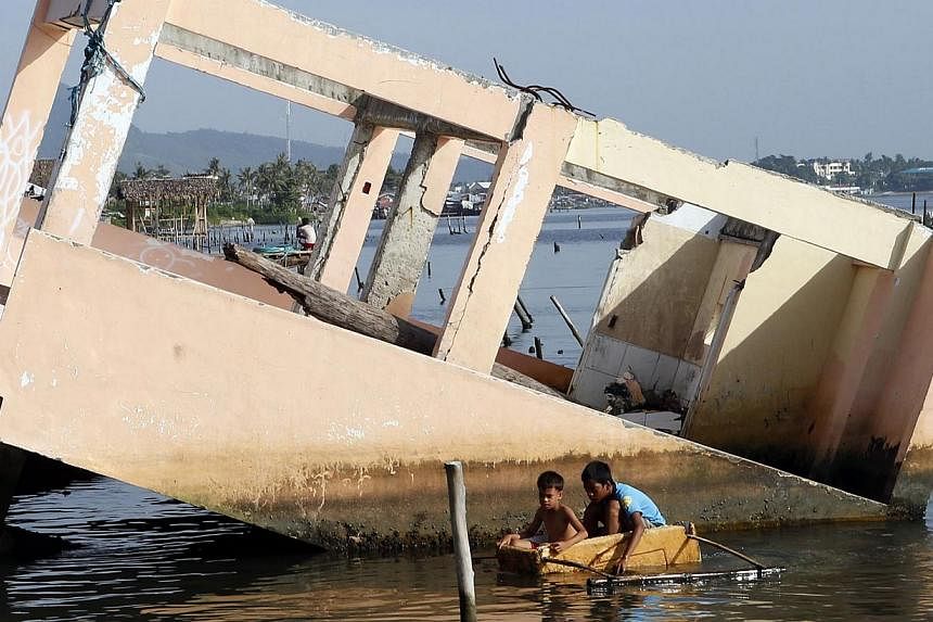 Boys paddling on a makeshift boat made of a styrofoam box next to a house swept away by Typhoon Haiyan in Tacloban city. A year on, only 50 families out of over 14,500 families in evacuation centres have permanent housing. Tacloban city residents pas