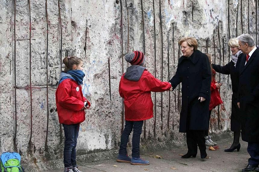 German Chancellor Angela Merkel (centre) shakes hands with children as she walks along a preserved segment of the Berlin Wall with Federal Government Commissioner for Culture Monika Gruetters (third, right), Berlin Mayor Klaus Wowereit (second, right