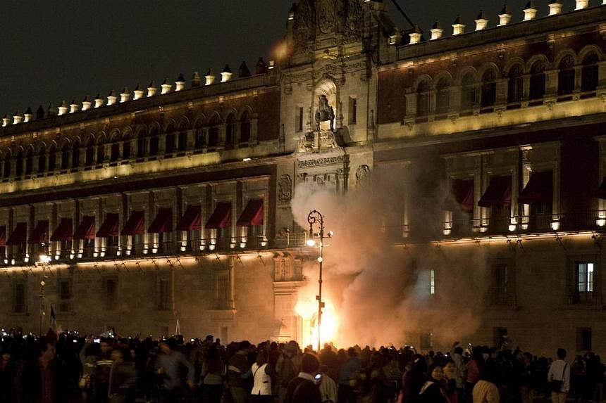 Demostrators set fire the door of the main entrance of te Mexican National Palace during a demostration in Mexico City on Nov 8, 2014, demanding justice from the Mexican goverment in the massacre of 43 missing students. -- PHOTO: AFP