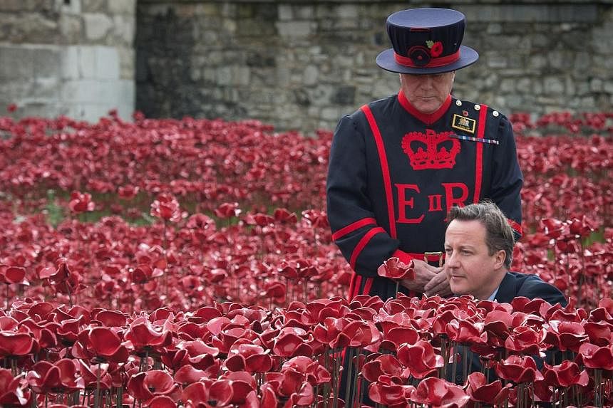A Yeomen Warder stands by as British Prime Minister David Cameron plants a poppy in the "Blood Swept Lands And Seas Of Red" installation by ceramic artist Paul Cummins and theatre stage designer Tom Piper, marking the centenary of the outbreak of the