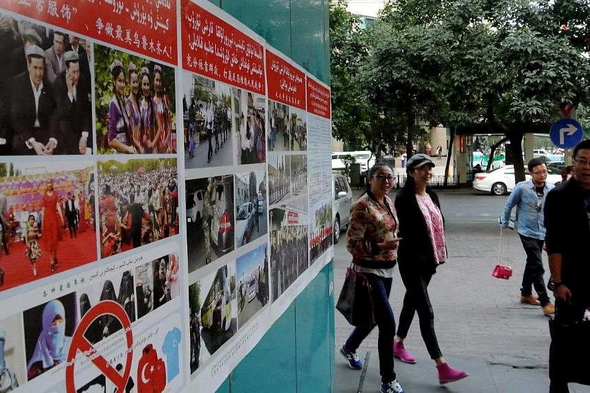 Pedestrians walk past anti-terror propaganda posters pasted along the streets of Urumqi, in western China's Xinjiang region on Sept 16, 2014.&nbsp;China has jailed almost two dozen people including "wild imams" who preach illegally in Xinjiang where 