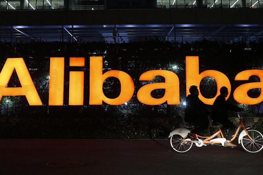 People ride a double bicycle past a logo of The Alibaba Group at the company's headquarters on the outskirts of Hangzhou, China, on Nov 10, 2014. -- PHOTO: REUTERS