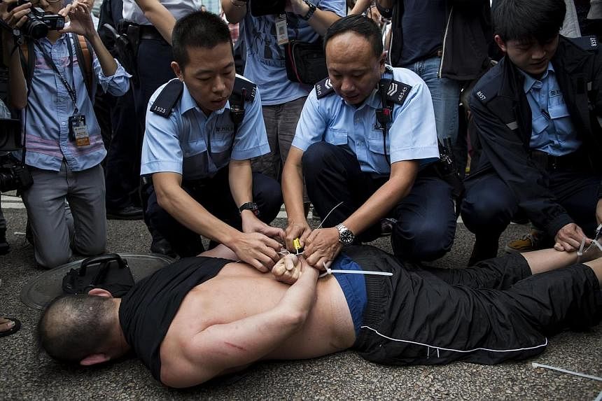 Police officers cut the plastic cords binding a man, who attempted to attack Hong Kong media magnate Jimmy Lai, after he was held by pro-democracy protesters in an occupied area in Hong Kong on Nov 12, 2014.&nbsp;-- PHOTO: REUTERS