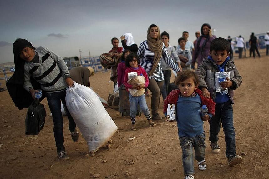 Kurdish Syrian refugees carry their belongings after crossing the Turkish-Syrian border near the southeastern town of Suruc in Sanliurfa province on Sept 25, 2014.&nbsp;Turkey is to issue work permits for some of the 1.5 million Syrian war refugees i