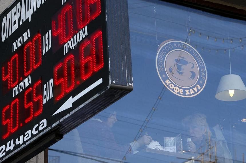 Women sit in a cafe, with a board showing currency exchange rates on display in the foreground, in Moscow, on Oct 8, 2014.-- PHOTO: REUTERS