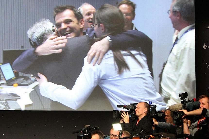 Journalists film near a giant screen featuring European Space Agency scientists celebrating after the announcement of the first-ever landing on a comet, done by European probe Philae, at theESA/ESOC in Darmstadt, western Germany, on Nov 12, 2014. -- 