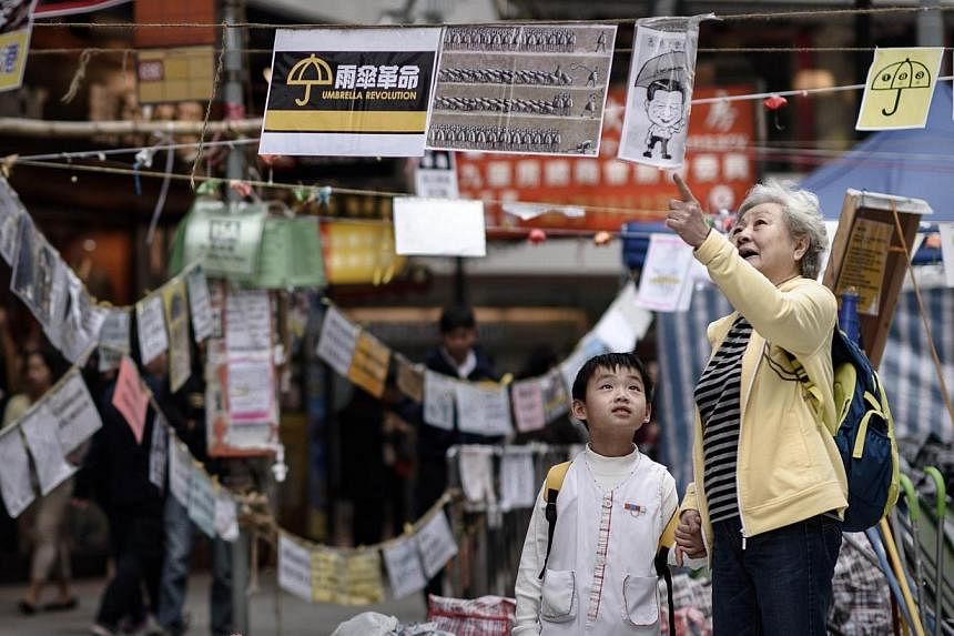 A elderly woman explains to a child the meaning of posters set up by pro-democracy protesters at a protest site in the Causeway Bay district of Hong Kong on Nov 14, 2014.&nbsp;Hong Kong warned Friday that "encouraging" growth in the third quarter may