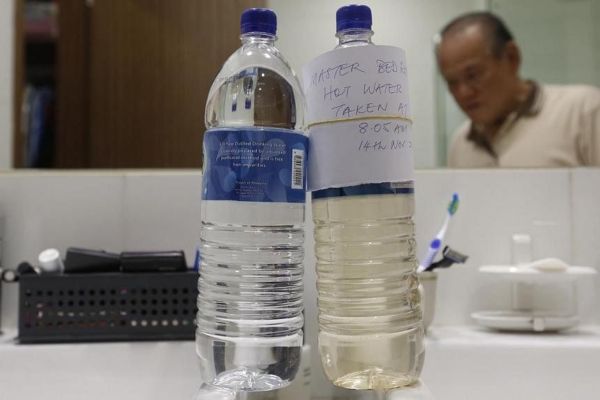 Retired trader Tong Chan Fui, 74, compares the bottle of rust-coloured water stored from the tap in his bedroom toilet with a clear one on 14 Nov 2014. -- ST PHOTO: KEVIN LIM