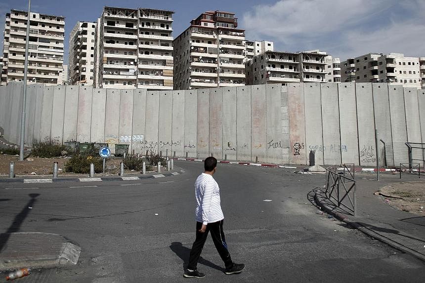 A Palestinian man walks past Israel's controversial separation barrier surrounding buildings of the Shuafat refugee camp in East Jerusalem on Nov 14, 2014.&nbsp;Israel will never agree to limit its construction activity in annexed east Jerusalem, For
