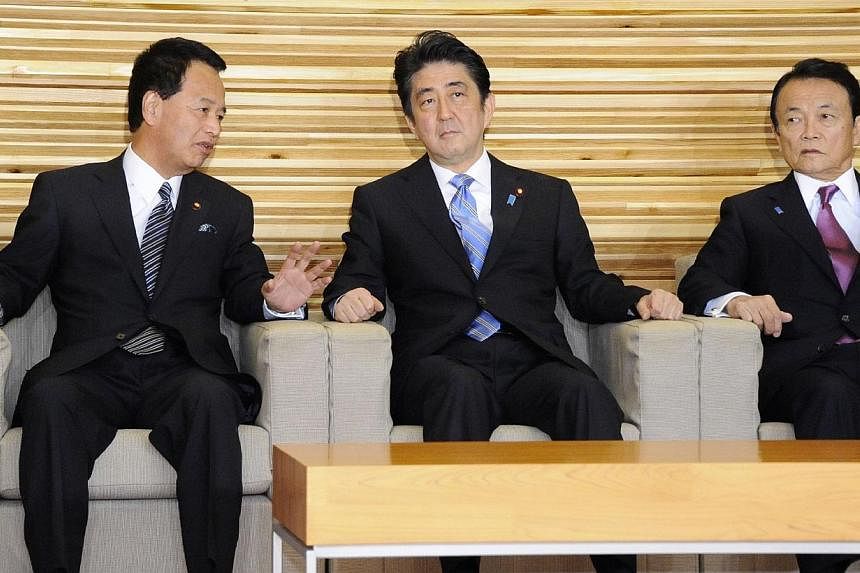 Japan's Prime Minister Shinzo Abe (centre) listens to Economic Revitalization Minister Akira Amari (left) at a cabinet meeting at the prime minister's official residence in Tokyo on Nov 18, 2014, while Finance Minister Taro Aso (right) looks on.&nbsp