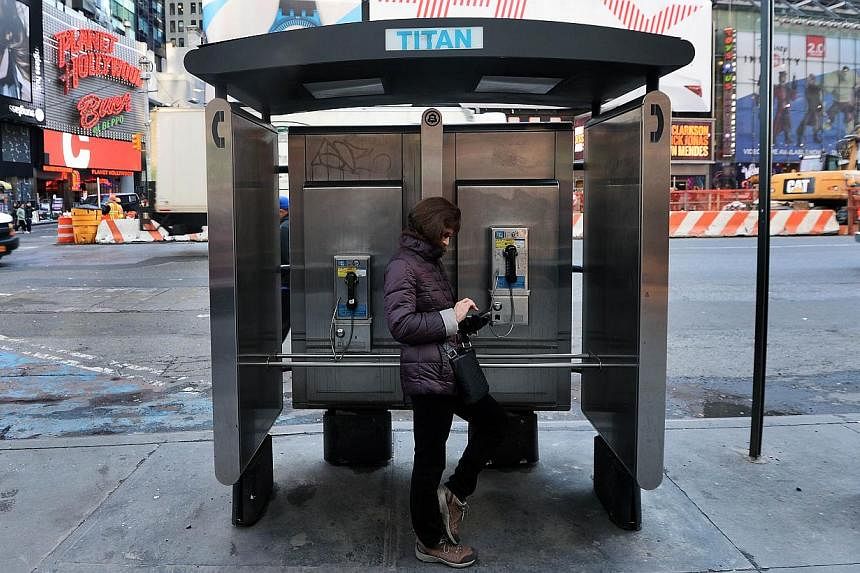 A woman uses her cell phone while leaning on a public phone booth in New York. Thousands of high-tech terminals offering free Wi-Fi and other services will soon replace the city's remaining fleet of seldom-used pay phones. -- PHOTO: AFP&nbsp;