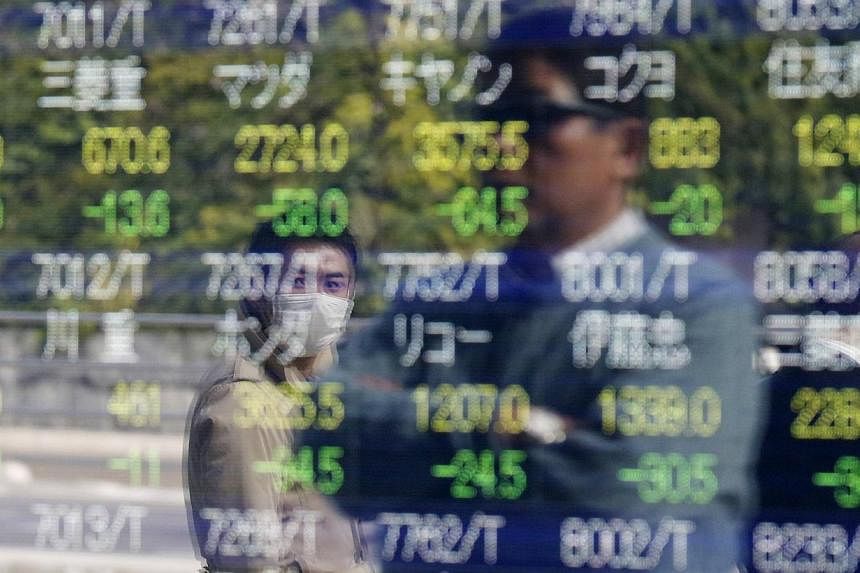Passers-by are reflected on an electronic stock quotation board outside a brokerage in Tokyo, on Nov 17, 2014. -- PHOTO: REUTERS