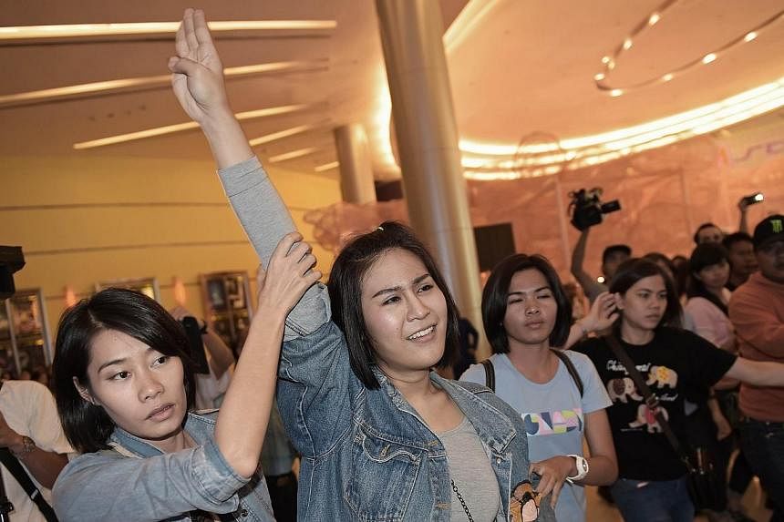 A Thai student (centre) flashes a three-finger salute, an unofficial symbol of resistance against the army's May coup, as she is escorted out of a cinema hall by plainclothes female police officers in Bangkok on Nov 20, 2014. -- PHOTO: AFP