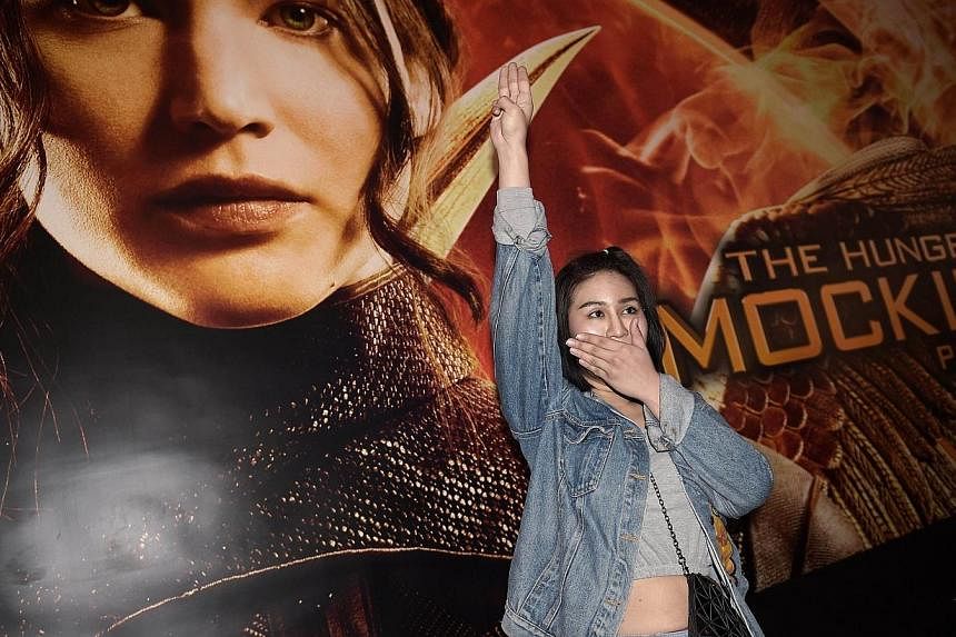 A Thai student flashes a three-finger salute, an unofficial symbol of resistance against the army's May coup, as she stands by a poster of the latest Hunger Games film, at a cinema hall in Bangkok on Nov 20, 2014.&nbsp;-- PHOTO: AFP