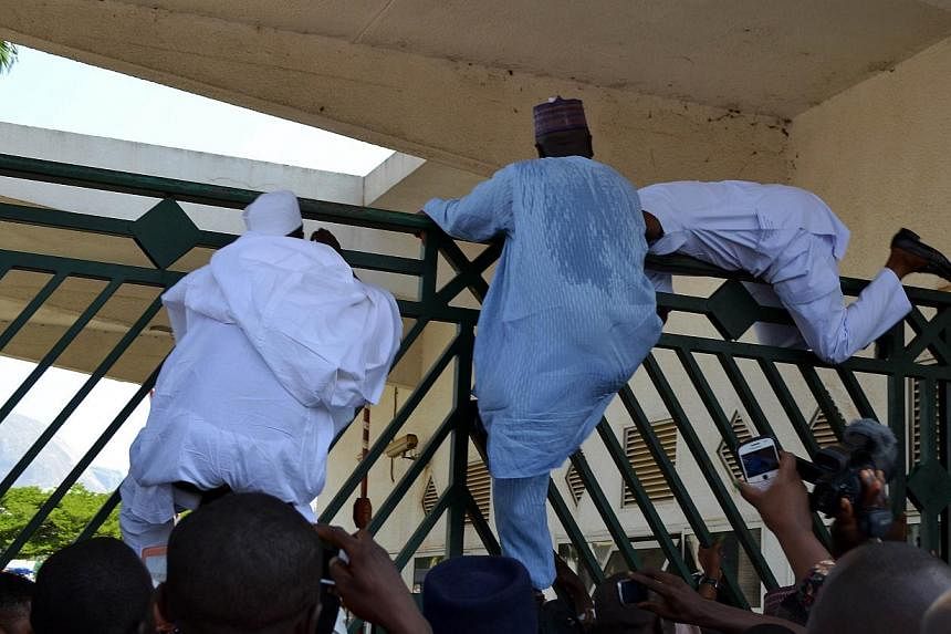 Nigerian parliament members climb the assembly gate closed by security forces in Abuja on Nov 20, 2014. Nigerian police fired teargas inside parliament, apparently trying to block opposition lawmakers, including the speaker of the lower house, from e