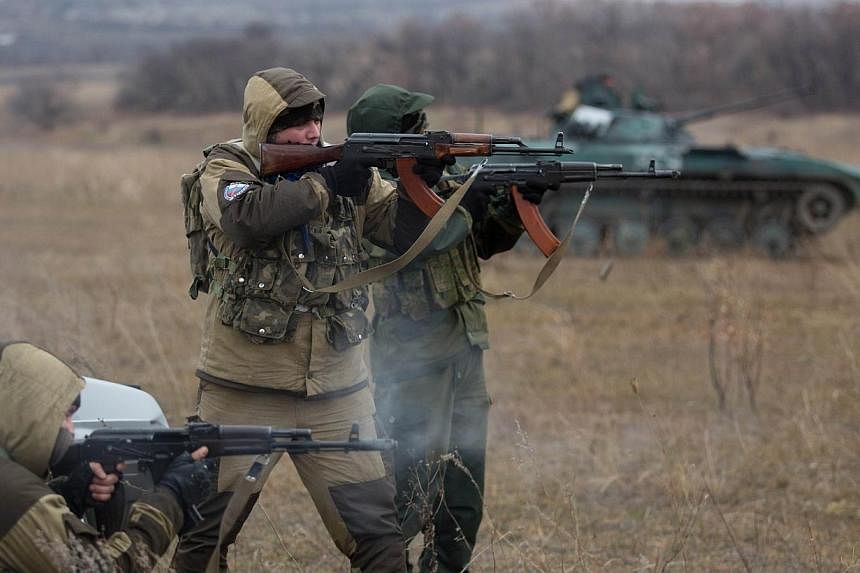 Pro-Russian militants fire their Kalachnikov asssault rifles near an tank taken from Ukrainian forces during fighting in August, as they test fire in an open field, in the eastern Ukrainian town of Ilovaisk on Nov 18, 2014. -- PHOTO: AFP&nbsp;