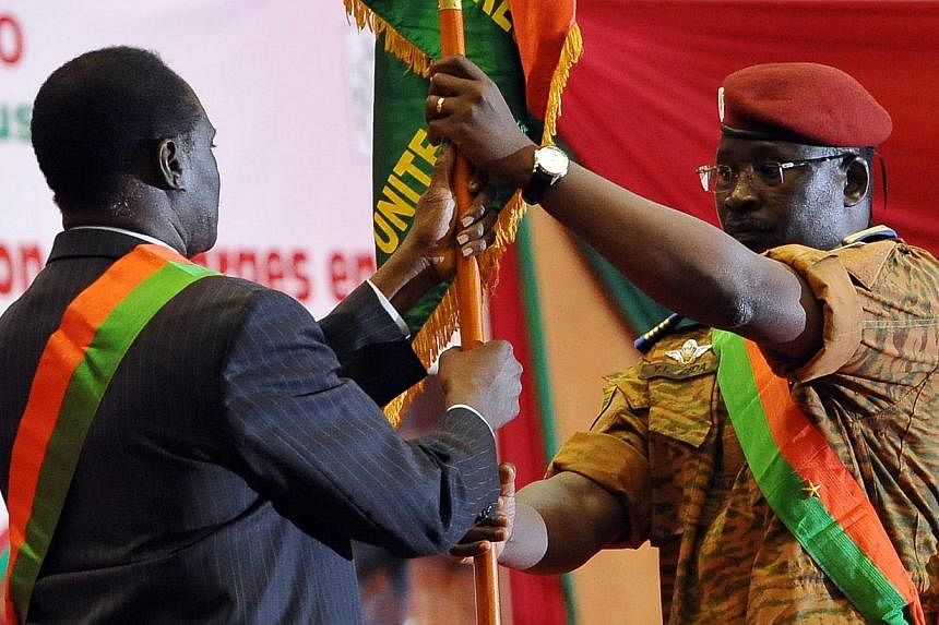 Lt-Col Isaac Zida (right) presenting the Burkinabe flag to interim civilian President Michel Kafando on Nov 21, 2014, at a stadium in Ouagadougou for a ceremony attended by six African heads of state. -- PHOTO: AFP