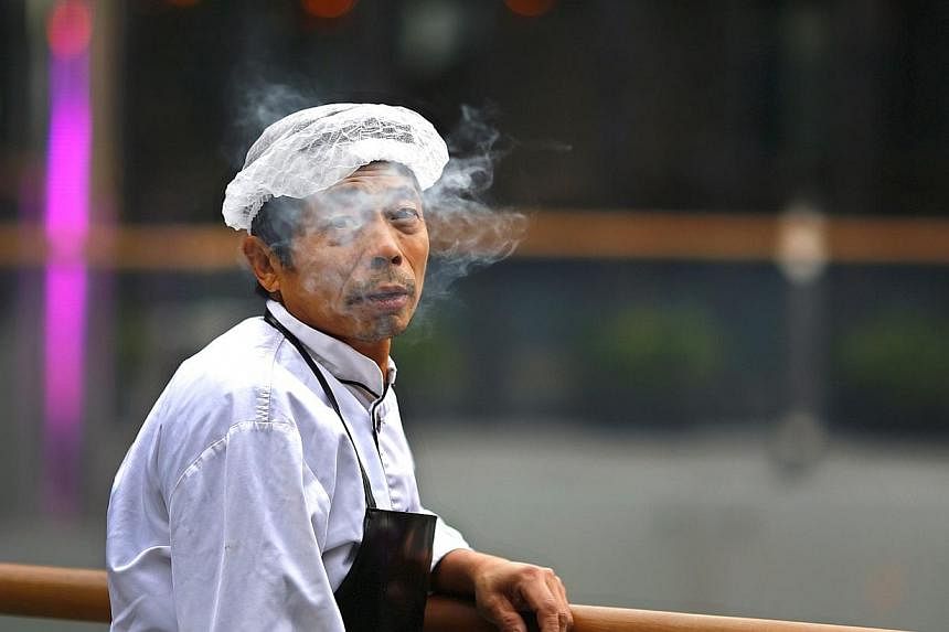 A man looks up as he smokes at Sanlitun Village, a shopping area in Beijing, Nov 23, 2014.&nbsp;China's capital on Friday passed a smoking ban for all indoor public places and offices, state media reported. -- PHOTO: REUTERS