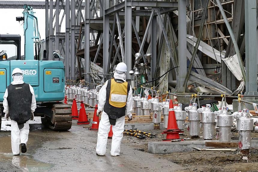 Workers wearing radiation protective gear stand outside of the No. 4 reactor building at Tepco's tsunami-crippled Fukushima Daiichi nuclear power plant in Fukushima prefecture on Nov 12, 2014. -- PHOTO: REUTERS