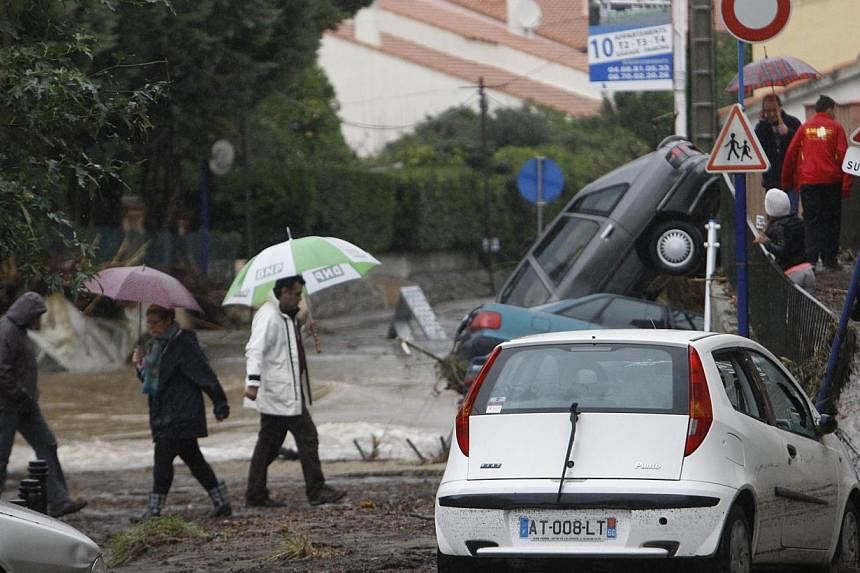 People walk in mud-covered streets near damaged cars after the river Massane flooded the city of Argeles-sur-Mer, southern France, due to heavy rains on Nov 30, 2014. -- PHOTO: AFP