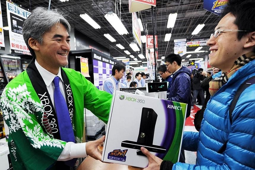 This file picture taken on Nov 20, 2010 shows Microsoft Japan Interactive Entertainment Business general manager Takashi Sensui (left) delivering the company's Xbox 360 Kinect to a Japanese customer (right) at a shop in the electronic goods district 
