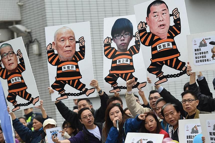 Anti Occupy Central movement protesters hold placards and shout slogans as the movement founders Benny Tai, Chan Kin-man and Chu Yiu-ming (not seen) prepare to surrender to police in Hong Kong on Dec 3, 2014. -- PHOTO: AFP