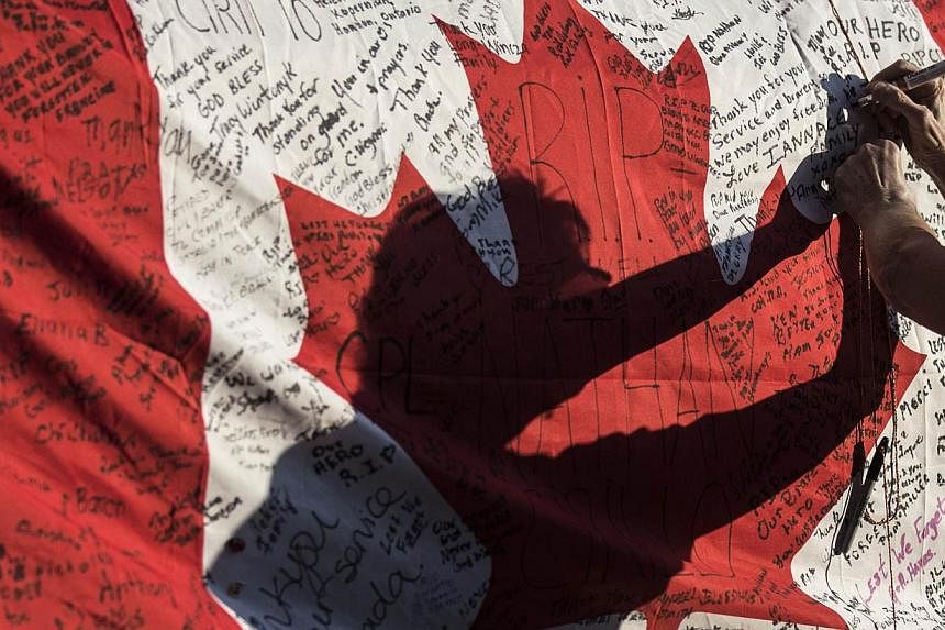 A woman writes a message on a Canadian flag at a makeshift memorial in honour of Cpl Nathan Cirillo, outside the Lieutenant-Colonel John Weir Foote Armoury, on Oct 24, 2014. -- PHOTO: REUTERS