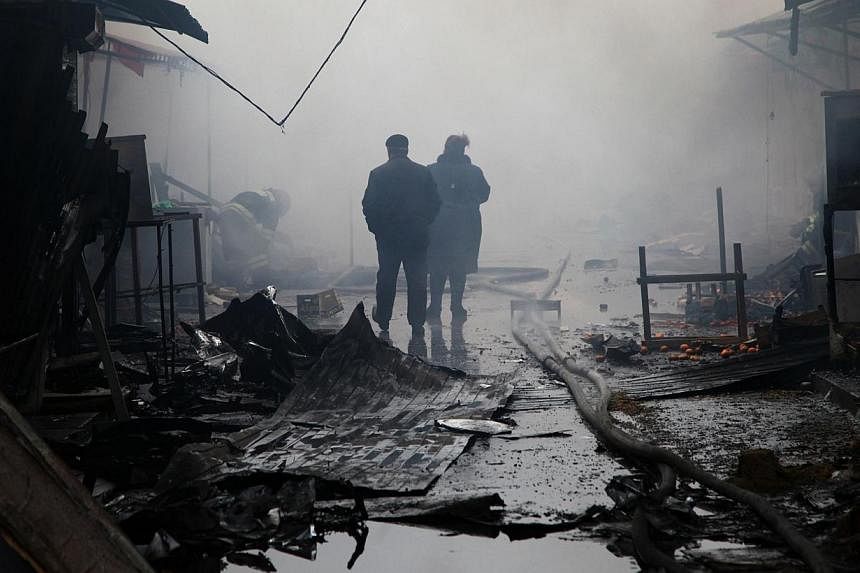People walk past burnt out kiosks at a street market close to a destroyed building housing the housing the local media known as the Press House, in central Grozny on December 4, 2014. -- PHOTO: AFP