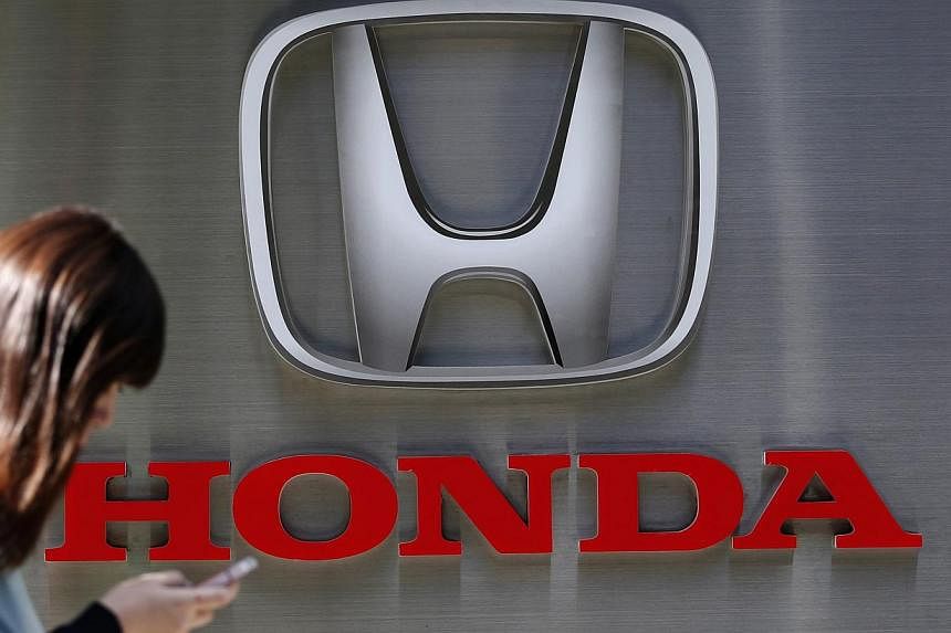 A woman using her mobile phone walks past a logo of Honda Motor Co outside the company's dealership in Tokyo on Oct 28, 2014. -- PHOTO: REUTERS