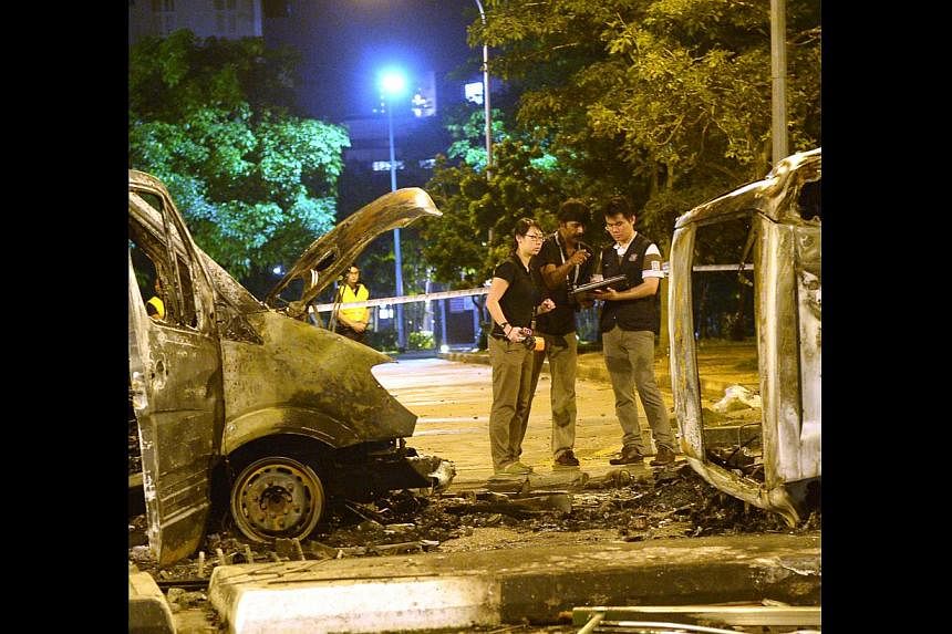 Police officers examining an ambulance and a police car that were burnt beyond recognition in Race Course Road, a day after the Little India riot on Dec 8 last year. -- ST FILE PHOTO