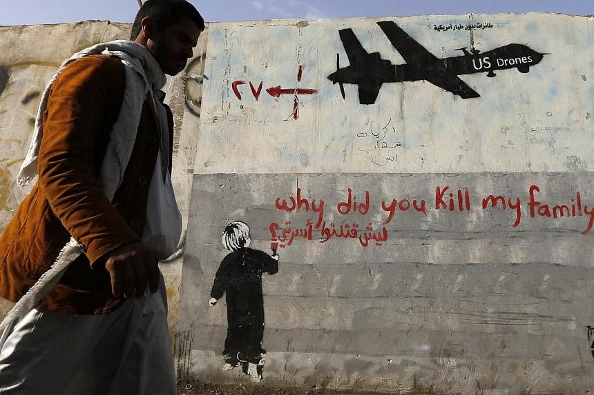 A man walks past a graffiti, denouncing strikes by U.S. drones in Yemen, painted on a wall in Sanaa on Nov 13, 2014. -- PHOTO: REUTERS