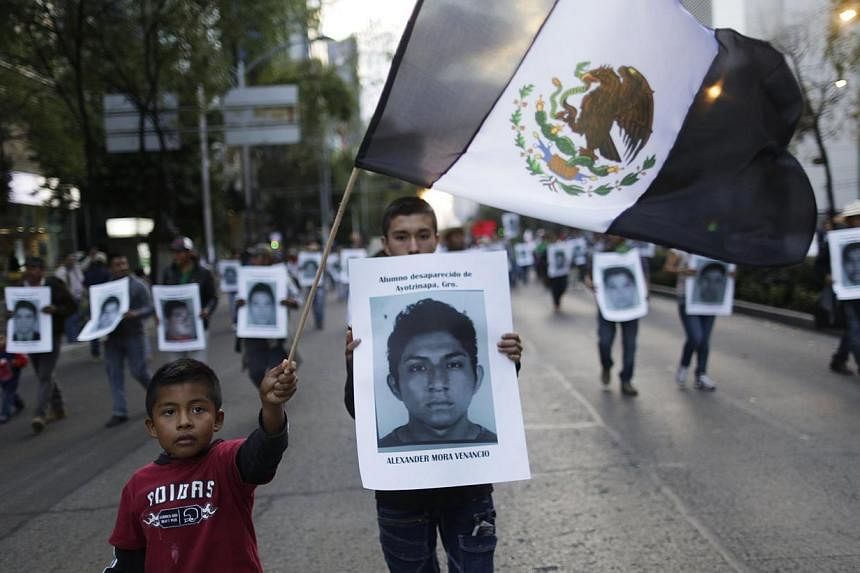A demonstrator carries a photograph of Alexander Mora Venancio, one of the 43 missing trainee teachers, as a boy waves a Mexican flag with its green and the red parts replaced with black as a sign of mourning, during a march in support of the student