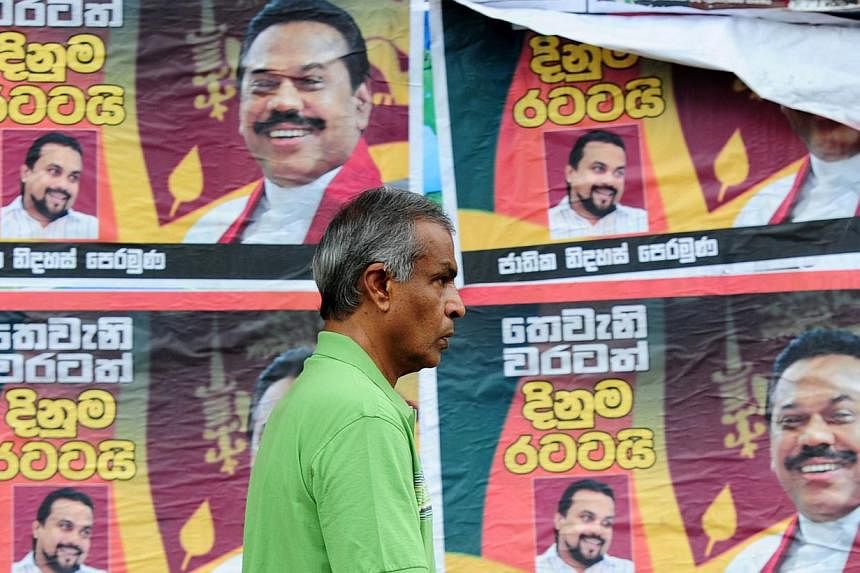 A Sri Lankan man walks past a billboard bearing portraits of President Mahinda Rajapakse in Colombo on Nov 19, 2014.&nbsp;Sri Lanka slashed cooking gas prices on Sunday just one day after the cost of diesel and petrol was also cut ahead of next month