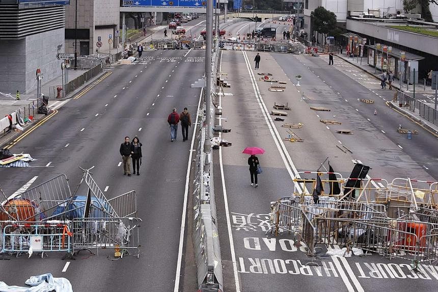 People walk past obstacles and barricades set up by pro-democracy protesters on a main road at the financial Central district in Hong Kong on Dec 7, 2014.&nbsp;Hong Kong pro-democracy protesters were thin on the ground on Dec 8, ahead of a possible m