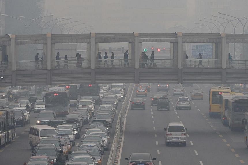 Pedestrians and commuters make their way through Beijing amid heavy smog. Projected global warming this century has slowed but is still at a severe rate, a scientific study showed on Monday. -- PHOTO: AFP&nbsp;