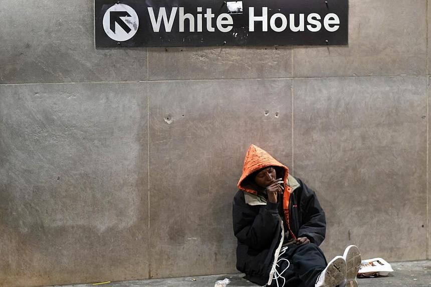 A homeless man sits under a sign giving directions to the White House at the entrance of the McPherson Metro Station in Washington, DC on Nov 25, 2014. -- PHOTO: AFP