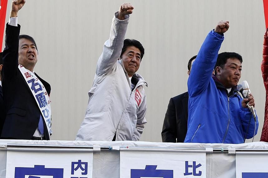 Japan's Prime Minister Shinzo Abe (centre) raises his fist with a candidate and supporters atop a van during a campaign for the Dec. 14 lower house election in Tokyo on Sunday December 7, 2014. On Tuesday, Abe announced that Apple would build one of 