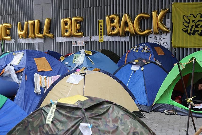 A protester reads a book in her tent at the main anti-government protest site next to a sign that reads "We Will Be Back" in the Admiralty district of Hong Kong on Dec 10, 2014. -- PHOTO: AFP