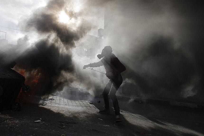 A Palestinian protester takes position near a burning tyre amidst tear gas fired by Israeli troops during clashes, following the funeral of Palestinian minister Ziad Abu Ein near the West Bank city of Ramallah on Dec 11, 2014. Thousands of mourners t