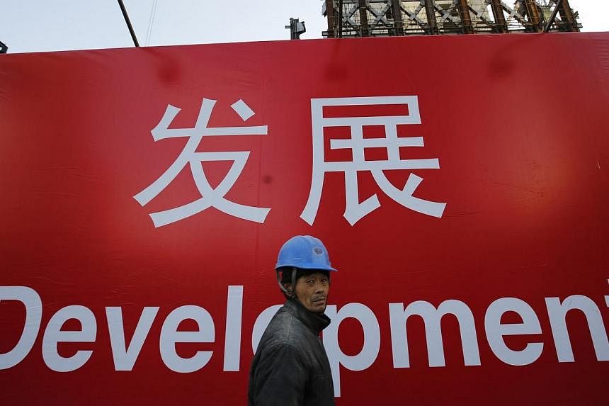 A worker walks past a propaganda slogan on a wall at a construction site in Beijing on Dec 12, 2014.&nbsp;China's economic growth could slow to 7.1 per cent in 2015 from an expected 7.4 per cent this year, held back by a sagging property sector, the 