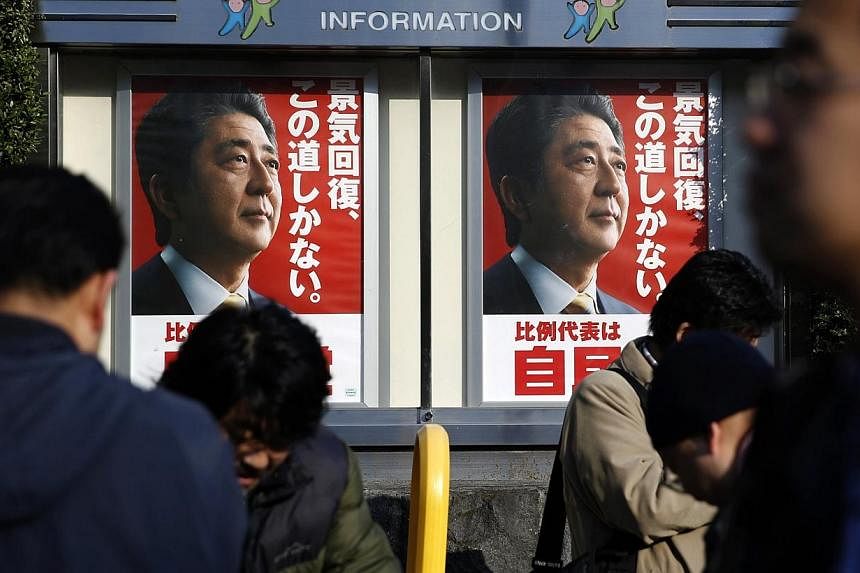 Posters of Japan's Prime Minister Shinzo Abe, who is also the leader of the ruling Liberal Democratic Party (LDP), are seen as members of media stand in front of the LDP headquarters in Tokyo on Dec 14, 2014. -- PHOTO: REUTERS