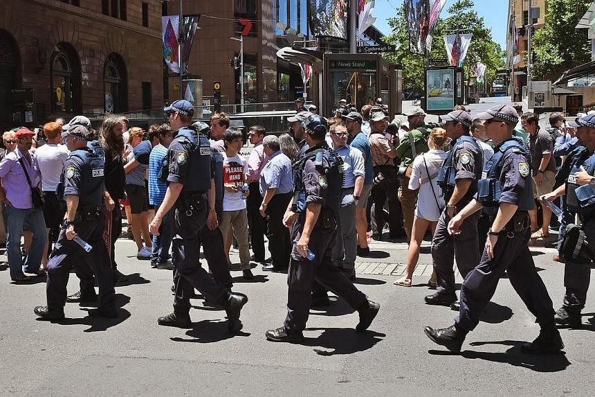 Police walk through Martin Place as spectators look on during a hostage siege in the central business district of Sydney on Dec 15, 2014.&nbsp;Singapore's Ministry of Foreign Affairs (MFA) has reminded Singaporeans in Sydney to take extra precaution 