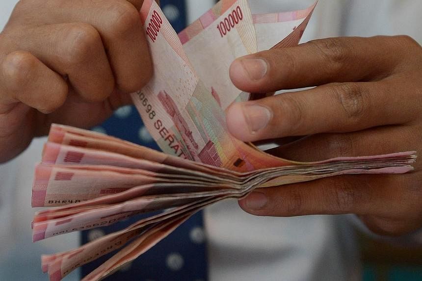 A teller counts Indonesian bank notes at a bank in Jakarta on Dec 15, 2014.&nbsp;Both the Malaysian ringgit and Indonesian rupiah have reached record lows at about the same time. -- PHOTO: AFP