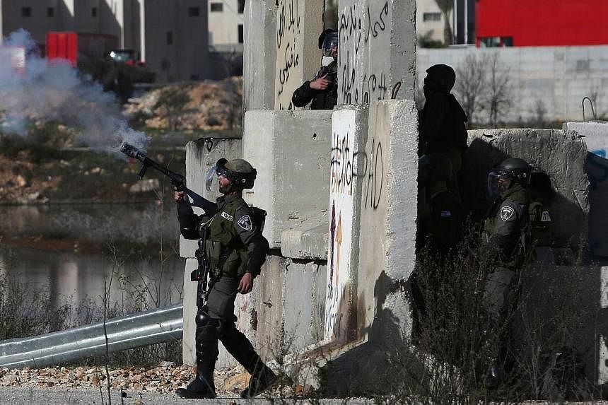 An Israeli soldier fires a smoke grenade towards students from Birzeit University (background) during clashes at the entrance of the Israeli Ofer military prison, near the West Bank village of Betunia, on Dec 13, 2014, following a march organized aga