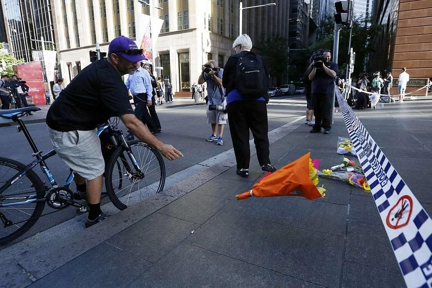 A man on a bicycle tosses a bouquet towards a police line restricting access to the site of the Sydney cafe siege after it ended on the early morning of Dec 16, 2014. -- PHOTO: REUTERS