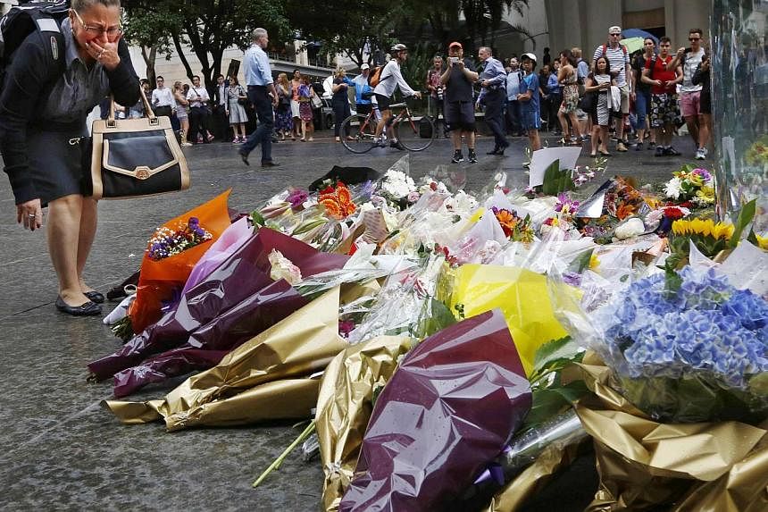 A woman reacts after placing a floral tribute for those who died in the Sydney cafe siege, near the site of the incident, in Martin Place on Dec 16, 2014. -- PHOTO: REUTERS