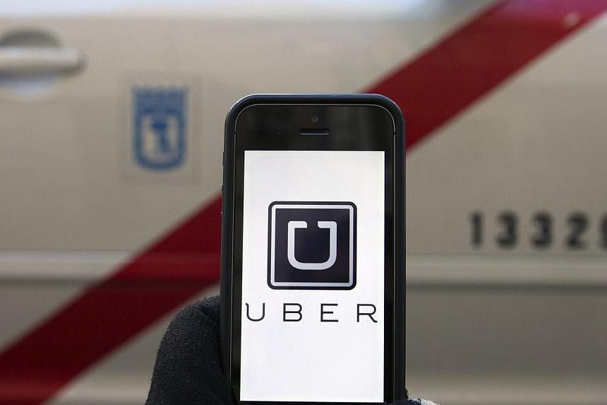 The logo of car-sharing service app Uber on a smartphone in front of a taxi is seen in this photo illustration taken in Madrid on Dec 10, 2014. -- COPY: REUTERS