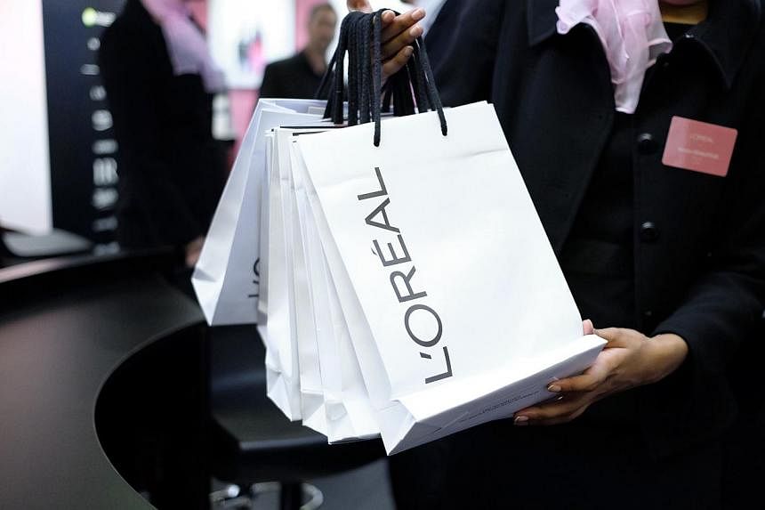 An employee gives bags to visitors at the stand of French cosmetics giant L'Oreal during the Actionaria shareholders fair in Paris on Nov 21, 2014. -- PHOTO: AFP