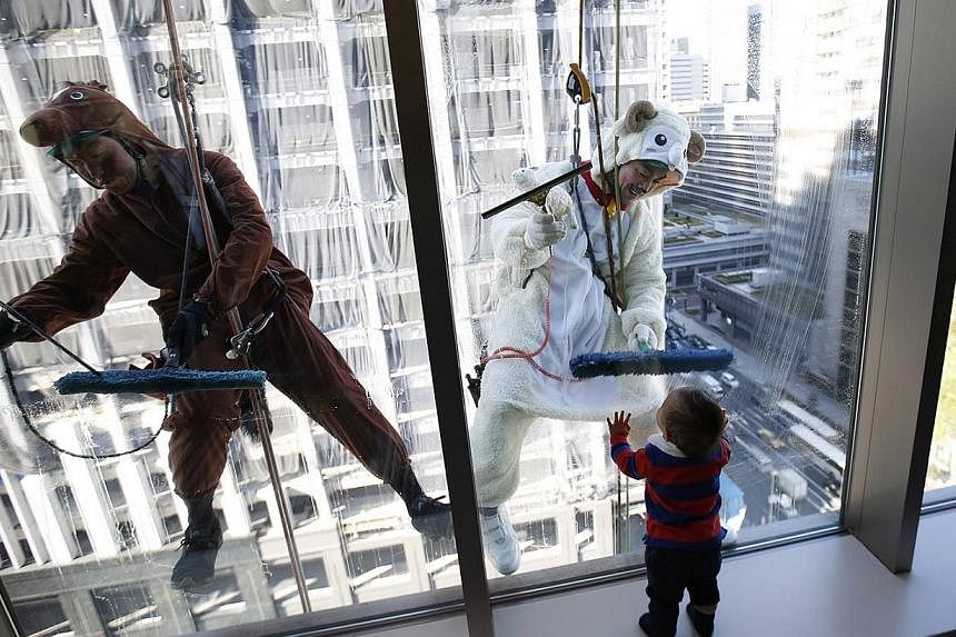 Window cleaners, dressed in horse (left) and sheep costumes featuring animals from the Chinese zodiac calendar, work during an event promoting the year-end and new year at a hotel in the business district of Tokyo on Dec 19, 2014. The year of 2014 is