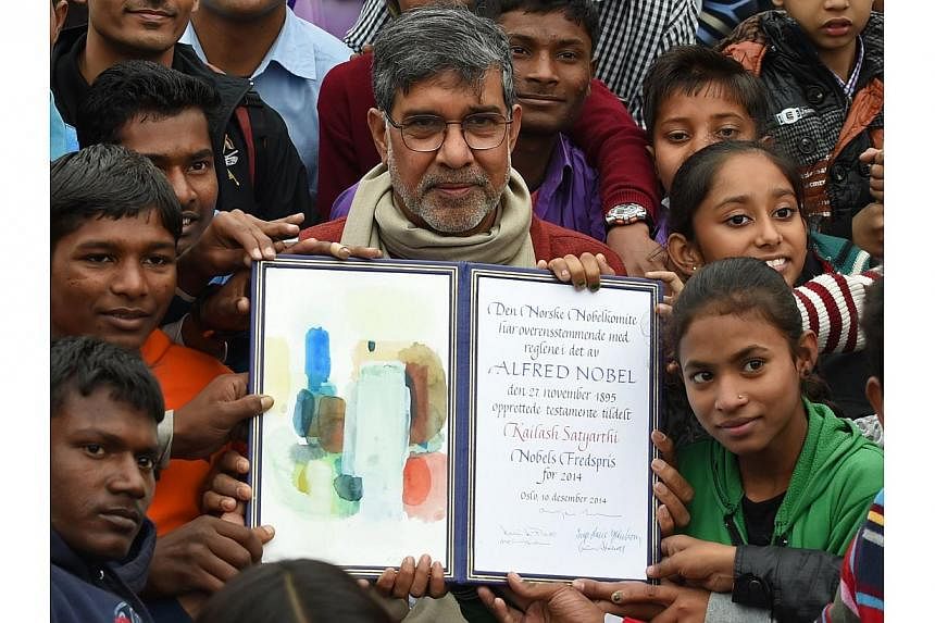 Indian Nobel Peace Prize winner Kailash Satyarthi holds up his Nobel diploma as he poses with children after paying tribute at Raj Ghat, the memorial for India's founding father Mahatma Gandhi, in New Delhi on Dec 14, 2014.&nbsp;Indian Nobel peace la